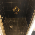 Black tiled shower with worn out looking tiles, dirt, and mold.